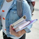 woman wearing blue denim jacket holding book